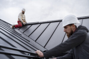 Roofing contractors wearing safety gear installing metal roof panels on a building, showcasing teamwork and professional roofing services